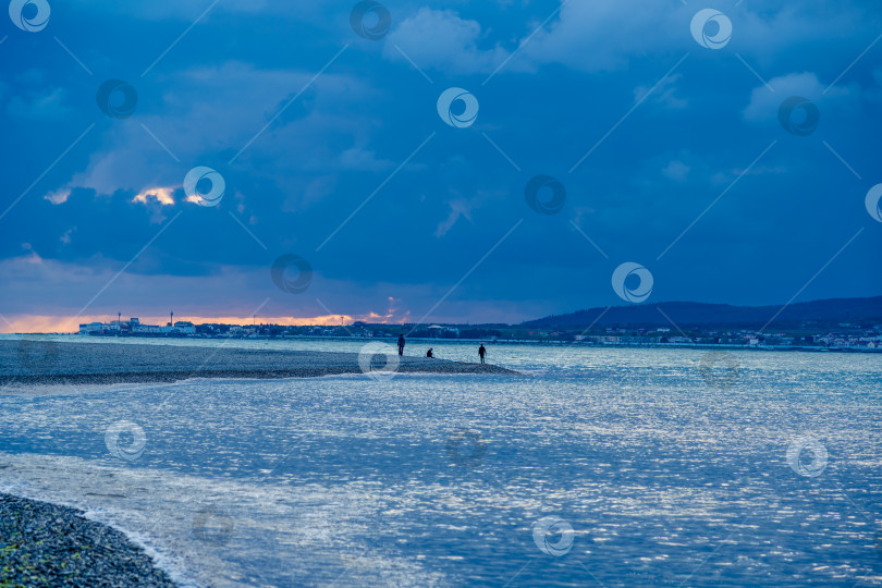 Скачать Курорт Геленджик. В вечерних сумерках мужчина сидит в одиночестве на берегу Геленджикской бухты. Кавказские горы на горизонте фотосток Ozero