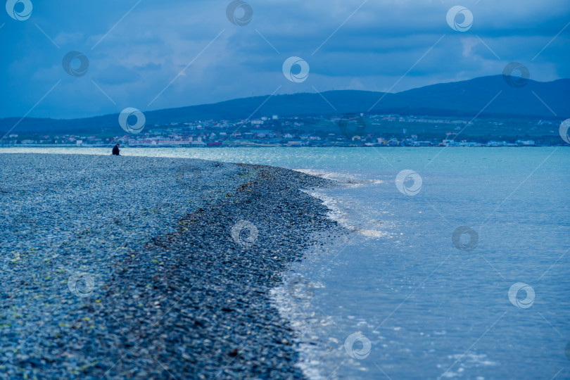 Скачать Курорт Геленджик. В вечерних сумерках мужчина сидит в одиночестве на берегу Геленджикской бухты. Кавказские горы на горизонте фотосток Ozero
