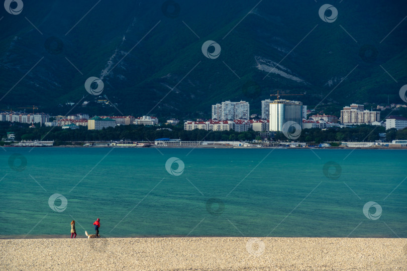 Скачать Курорт Геленджик. Закат. Мужчина и женщина с собакой прогуливаются по пляжу Геленджикской бухты на фоне Кавказских гор. фотосток Ozero