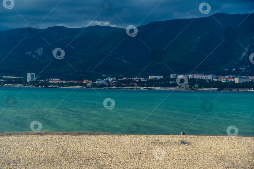 Скачать Курорт Геленджик. В вечерних сумерках мужчина сидит в одиночестве на берегу Геленджикской бухты. Кавказские горы на горизонте фотосток Ozero