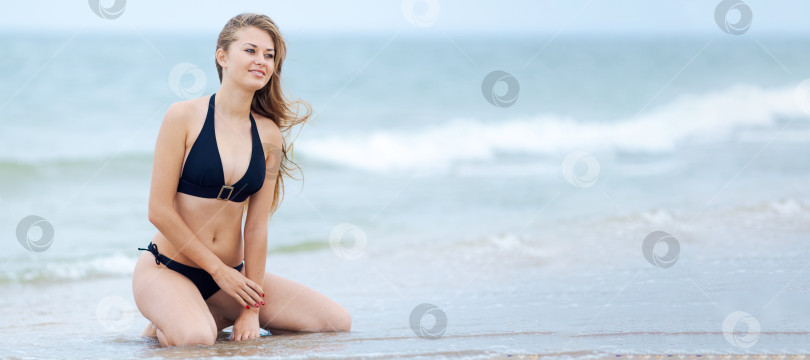 Скачать Женщина сидит на пляже в черном бикини фотосток Ozero