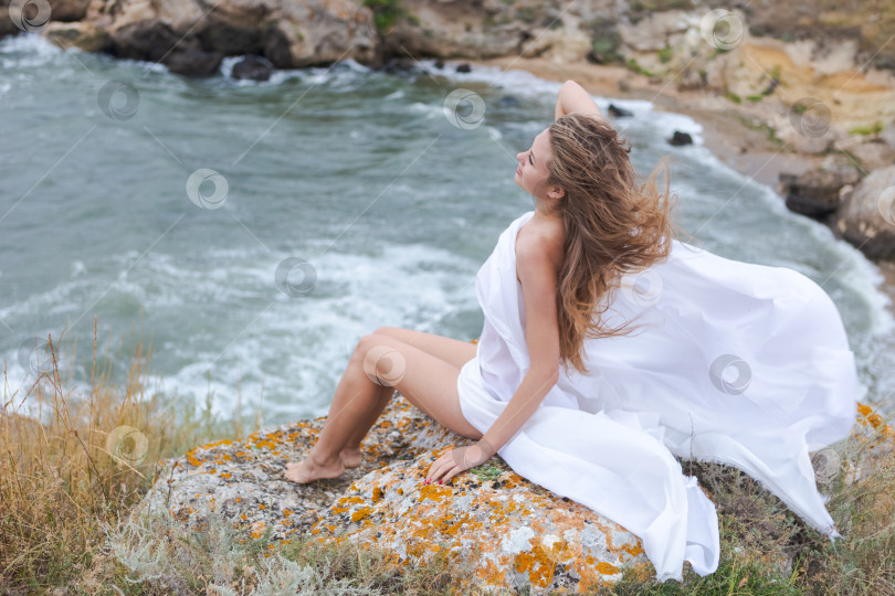 Скачать Женщина в белом платье сидит на скале у океана. фотосток Ozero