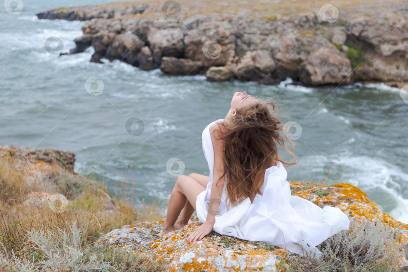 Скачать Женщина в белом платье сидит на скале у океана фотосток Ozero