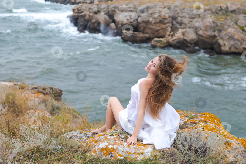 Скачать Женщина с длинными волосами сидит на скале у океана фотосток Ozero
