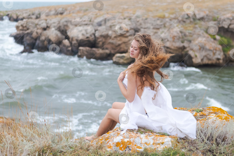 Скачать Женщина с длинными волосами сидит на скале у океана фотосток Ozero