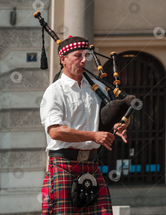 Скачать Мужчина, играющий на волынке в традиционном шотландском наряде, выступает на открытом воздухе фотосток Ozero