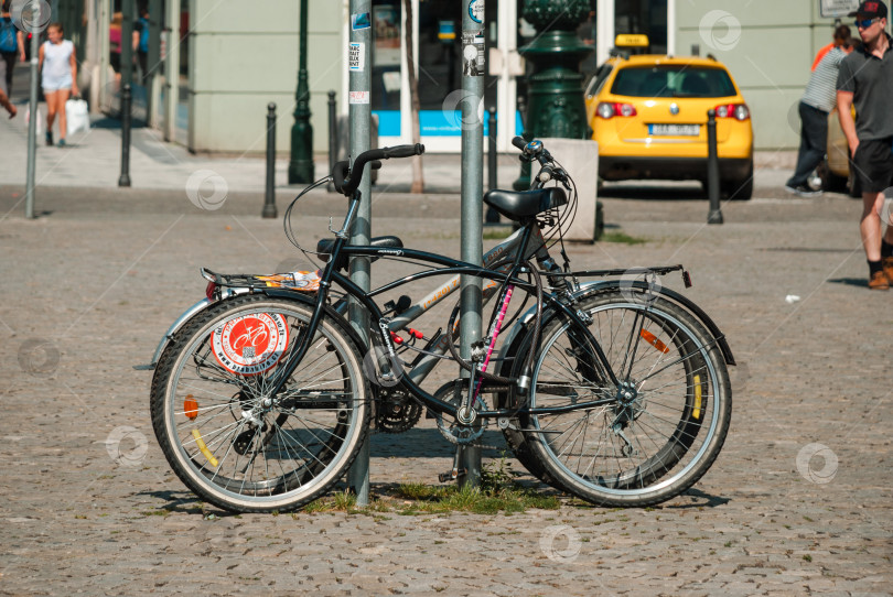 Скачать Черные велосипеды, привязанные к фонарному столбу на мощеной улице, и желтое такси неподалеку фотосток Ozero