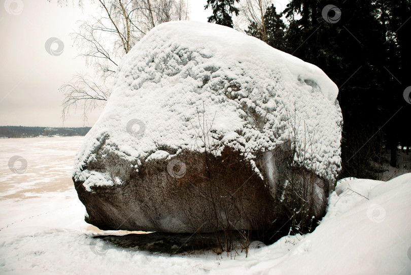 Скачать Заснеженный валун в зимнем пейзаже на фоне замерзшего озера и деревьев фотосток Ozero