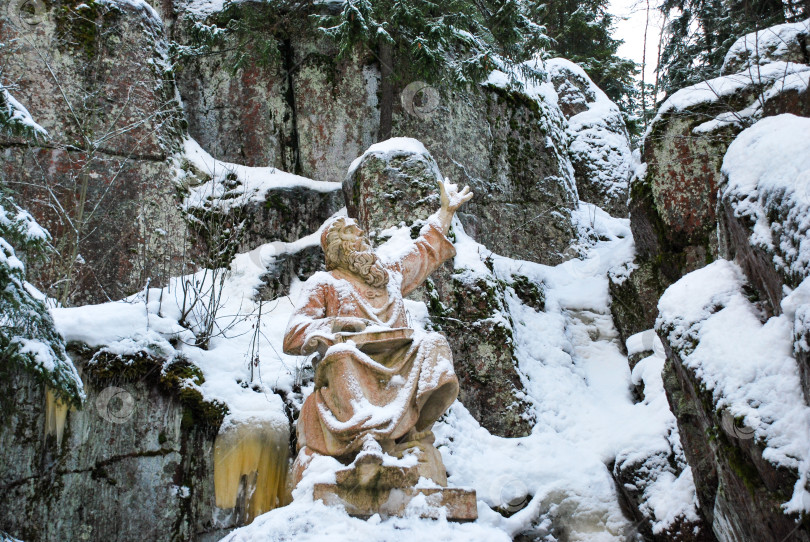 Скачать Заснеженная статуя бородатой фигуры на фоне скалистого лесного пейзажа фотосток Ozero