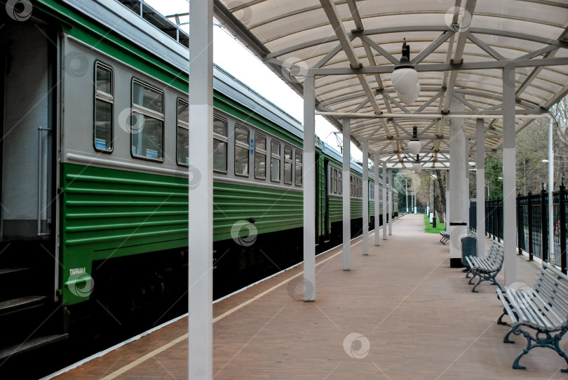 Скачать Пустая железнодорожная станция с зеленым пассажирским поездом в пасмурный день фотосток Ozero