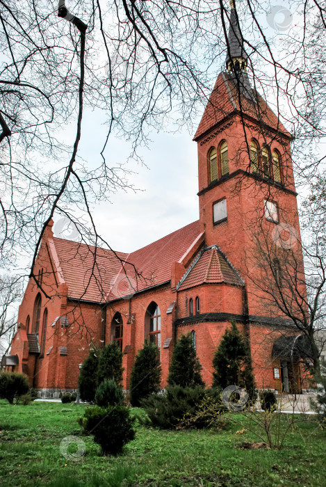 Скачать Историческая церковь из красного кирпича с башней, окруженная деревьями в безмятежной обстановке фотосток Ozero