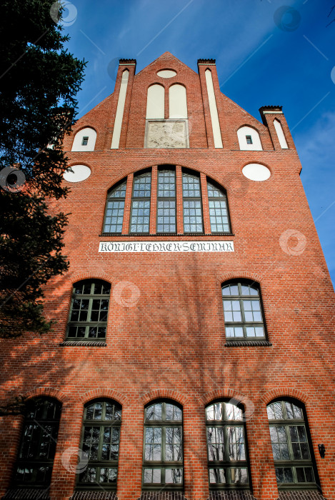 Скачать Историческое здание из красного кирпича с арочными окнами и двускатной крышей на фоне голубого неба фотосток Ozero