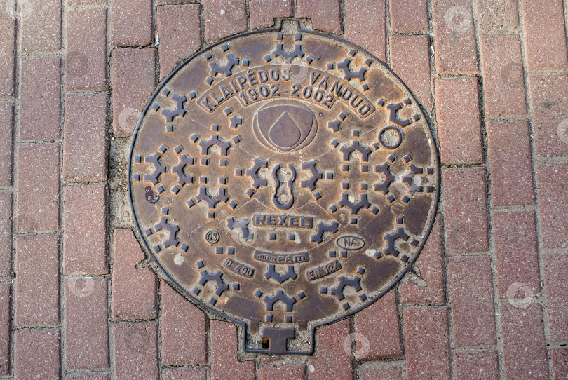 Скачать Замысловатый дизайн крышки канализационного люка на кирпичном тротуаре в Клайпеде, Литва фотосток Ozero