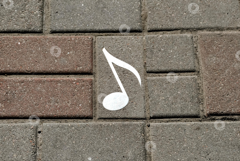 Скачать Белая музыкальная нота, нарисованная на сером и красном кирпиче тротуара в городских условиях фотосток Ozero