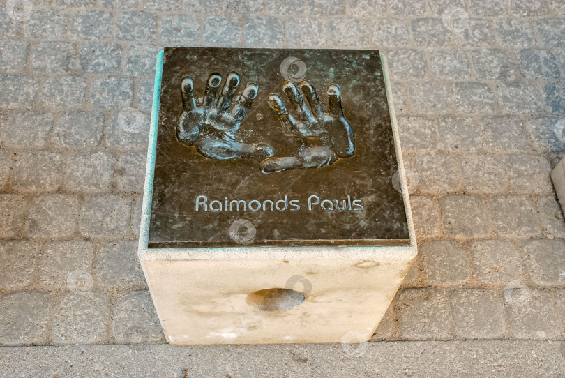 Скачать Бронзовая табличка с отпечатком руки Раймонда Паулса на мощеной дорожке фотосток Ozero