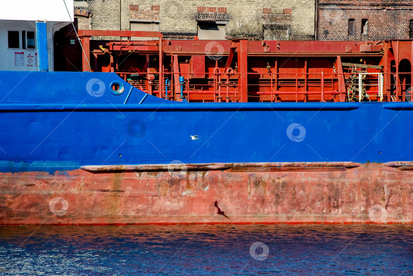 Скачать Яркое грузовое судно с красно-синим корпусом пришвартовалось в промышленной гавани фотосток Ozero
