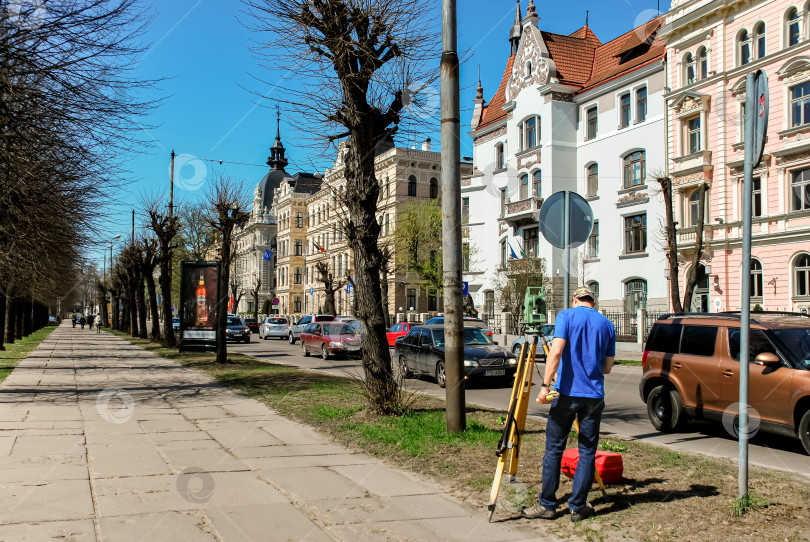 Скачать Мужчина-геодезист на оживленной городской улице с исторической архитектурой и ясным голубым небом фотосток Ozero