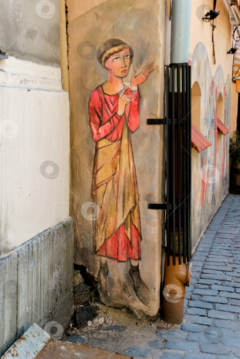 Скачать Красочная уличная художественная фреска в узком переулке, изображающая задумчивую фигуру в красном и желтом одеянии фотосток Ozero