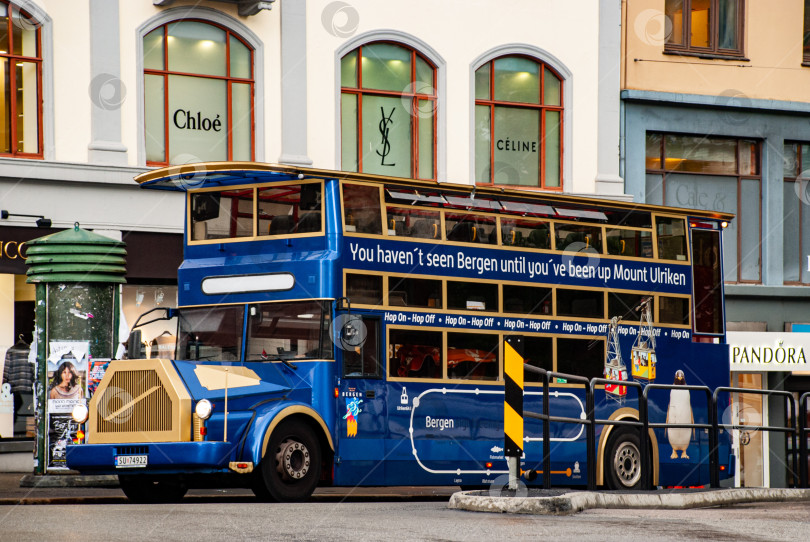 Скачать Голубой туристический двухэтажный автобус, курсирующий по улицам Бергена с вывеской "Гора Ульрикен" и торговыми бутиками фотосток Ozero
