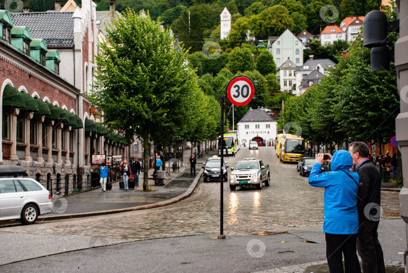 Скачать Уличная сцена в дождливый день в Бергене с туристами и дорожным знаком фотосток Ozero