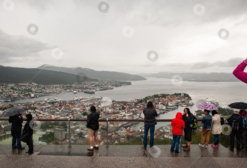 Скачать Затянутый облаками вид с Флойена на норвежский Берген, где туристы наслаждаются живописным пейзажем фотосток Ozero
