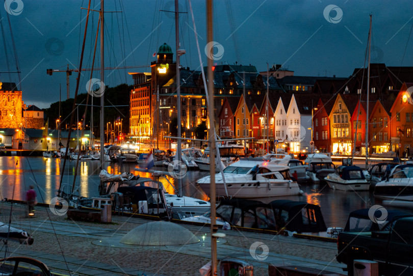 Скачать Вечерняя сцена на оживленной набережной марины с красочными зданиями и лодками фотосток Ozero