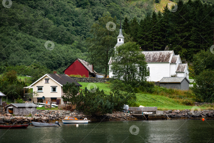 Скачать Очаровательная деревушка с белой церковью, домами и лодками, окруженная пышной зеленью, на берегу безмятежного озера фотосток Ozero