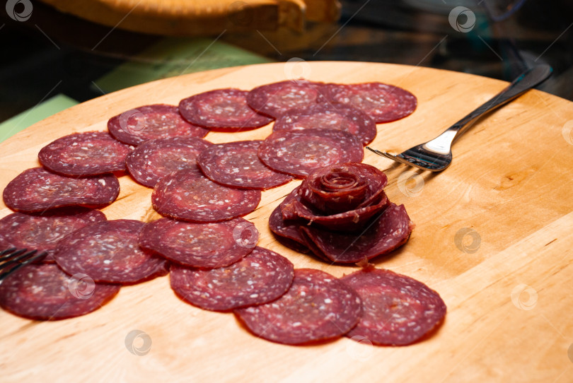 Скачать Нарезанная ломтиками салями на деревянной доске с оригинальным розовым гарниром фотосток Ozero