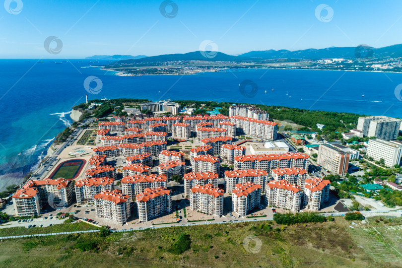 Скачать Панорама курорта Геленджик в солнечный день. На переднем плане многоэтажные здания. Маяк и вход в Геленджикскую бухту. Вид с высоты птичьего полета. фотосток Ozero