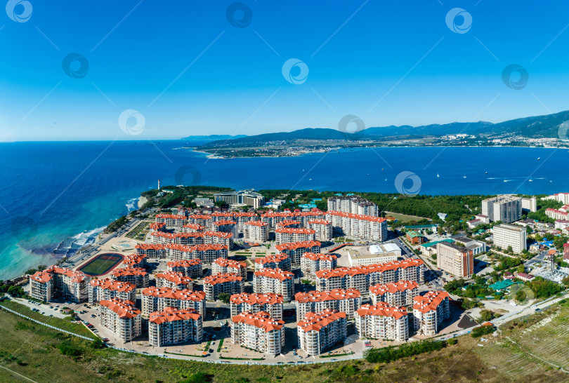 Скачать Панорама курорта Геленджик в солнечный день. На переднем плане многоэтажные здания. Маяк и вход в Геленджикскую бухту. Вид с высоты птичьего полета. фотосток Ozero