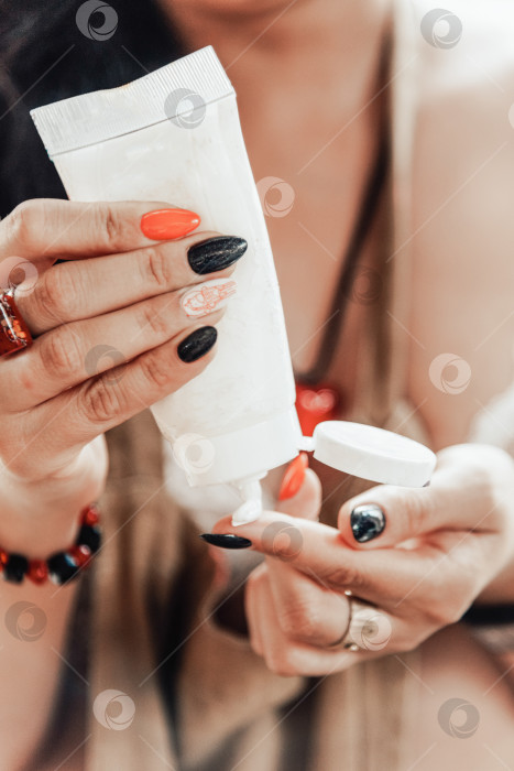 Скачать Женщина держит в руке тюбик с кремом и наносит увлажняющий крем на красивые руки фотосток Ozero