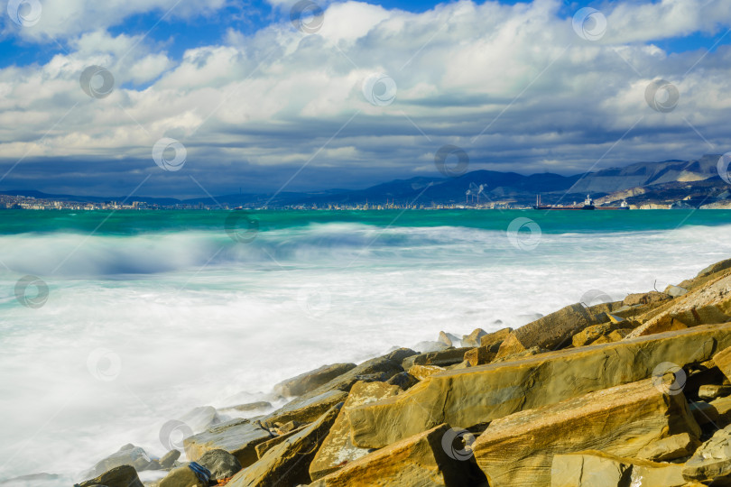 Скачать Курорт Кабардинка. Большие зеленые штормовые волны в белой пене. На заднем плане - порт Новороссийск и Кавказские горы. Большие камни на берегу. Фото с длительной выдержкой фотосток Ozero