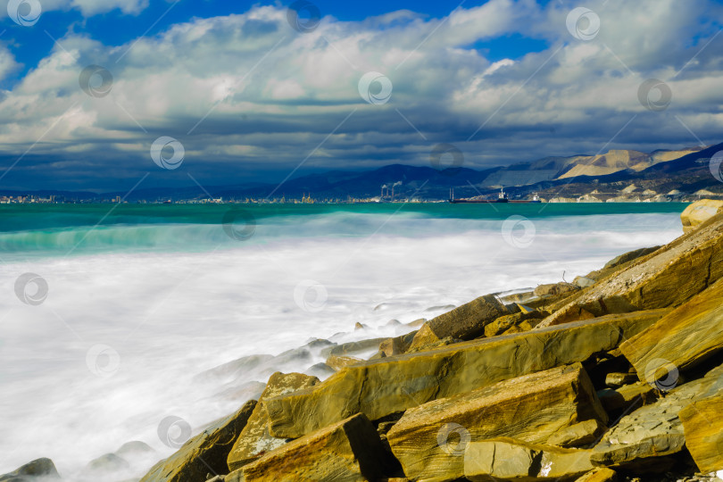 Скачать Курорт Кабардинка. Большие зеленые штормовые волны в белой пене. На заднем плане - порт Новороссийск и Кавказские горы. Большие камни на берегу. Фото с длительной выдержкой фотосток Ozero