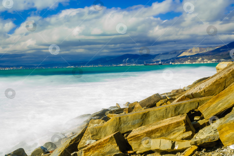 Скачать Курорт Кабардинка. Большие зеленые штормовые волны в белой пене. На заднем плане - порт Новороссийск и Кавказские горы. Большие камни на берегу. Фото с длительной выдержкой фотосток Ozero