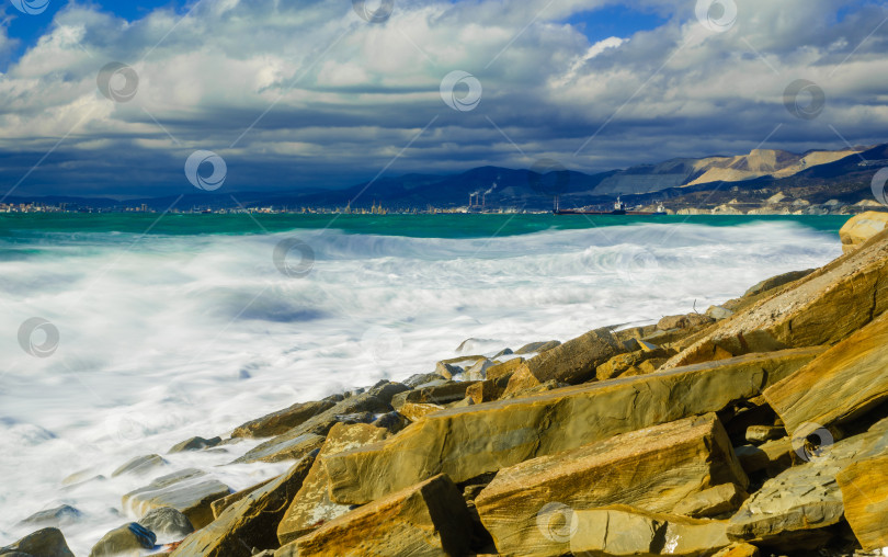 Скачать Курорт Кабардинка. Большие зеленые штормовые волны в белой пене. На заднем плане - порт Новороссийск и Кавказские горы. Большие камни на берегу. Фото с длительной выдержкой фотосток Ozero