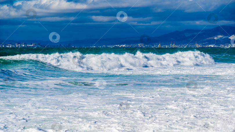 Скачать Курорт Кабардинка. Большие зеленые штормовые волны в белой пене накатываются на каменистый пляж Кабардинки. На заднем плане - порт Новороссийск и Кавказские горы. фотосток Ozero