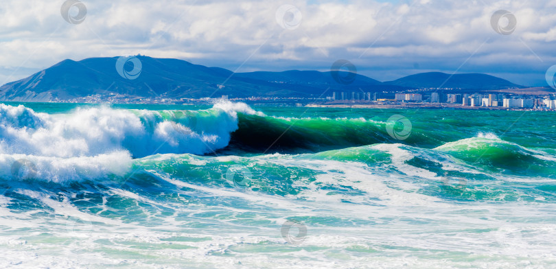 Скачать Курорт Кабардинка. Черное море. Большие штормовые волны изумрудного цвета накатывают на берег. Множество брызг и пены. Порт Новороссийск и Кавказские горы на горизонте фотосток Ozero