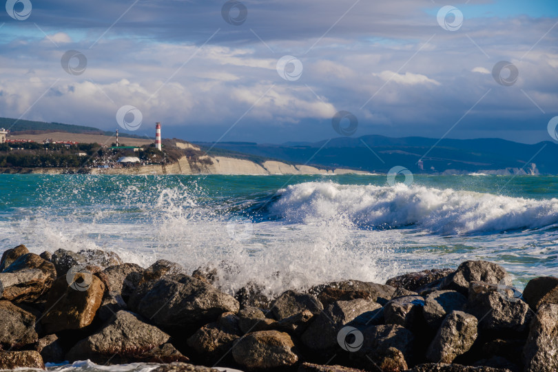 Скачать Курорт Геленджик. На фоне геленджикского маяка катятся большие зеленые штормовые волны. Маяк стоит на высоком утесе. На переднем плане видны большие камни фотосток Ozero