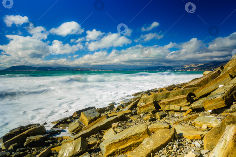 Скачать Курорт Кабардинка. Большие зеленые штормовые волны в белой пене. На заднем плане - порт Новороссийск и Кавказские горы. Большие камни на берегу. Фото с длительной выдержкой фотосток Ozero