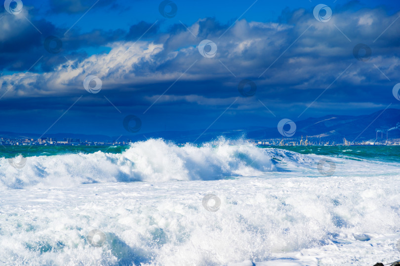 Скачать Курорт Кабардинка. Большие зеленые штормовые волны в белой пене накатываются на каменистый пляж Кабардинки. На заднем плане - порт Новороссийск и Кавказские горы. фотосток Ozero