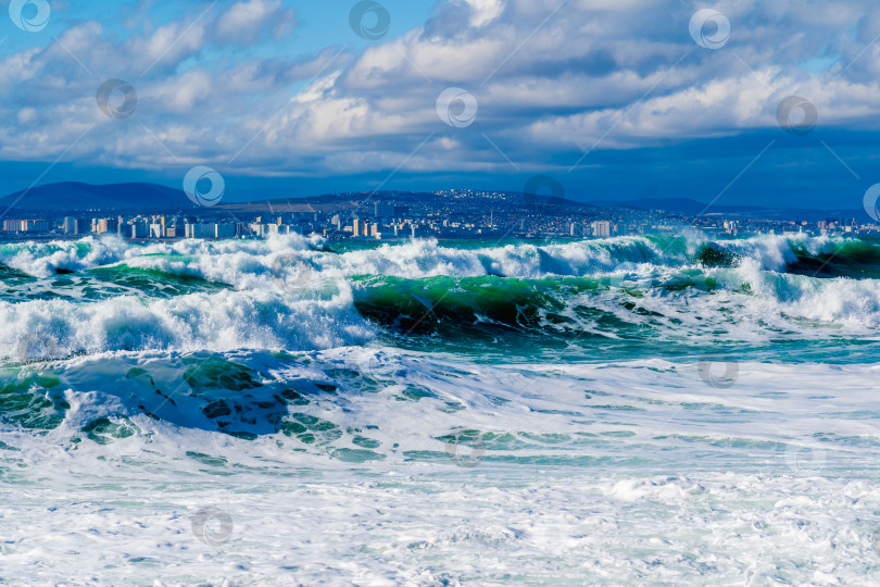 Скачать Курорт Кабардинка. Черное море. Большие штормовые волны изумрудного цвета накатывают на берег. Множество брызг и пены. Порт Новороссийск и Кавказские горы на горизонте фотосток Ozero