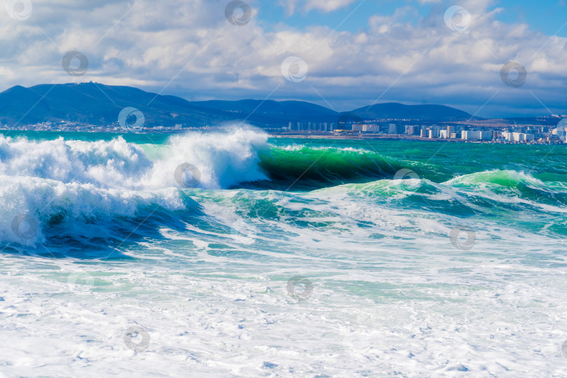 Скачать Курорт Кабардинка. Черное море. Большие штормовые волны изумрудного цвета накатывают на берег. Множество брызг и пены. Порт Новороссийск и Кавказские горы на горизонте фотосток Ozero