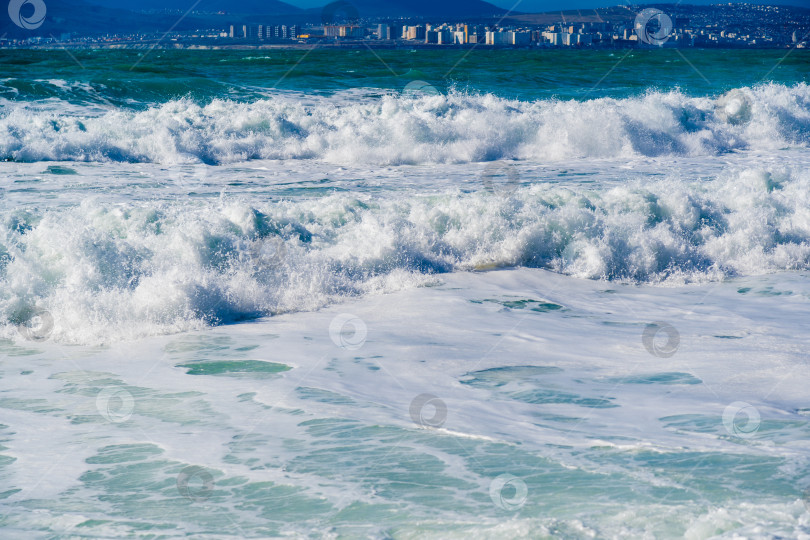 Скачать Курорт Кабардинка. Большие зеленые штормовые волны в белой пене накатываются на каменистый пляж Кабардинки. На заднем плане - порт Новороссийск и Кавказские горы. фотосток Ozero