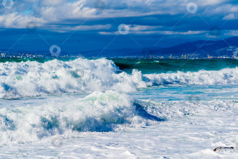 Скачать Курорт Кабардинка. Черное море. Большие штормовые волны изумрудного цвета накатывают на берег. Множество брызг и пены. Порт Новороссийск и Кавказские горы на горизонте фотосток Ozero