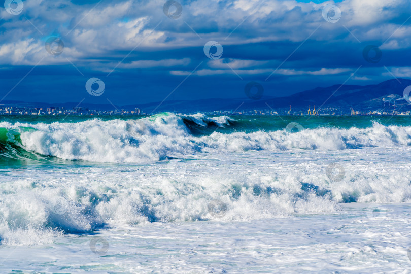 Скачать Курорт Кабардинка. Черное море. Большие штормовые волны изумрудного цвета накатывают на берег. Множество брызг и пены. Порт Новороссийск и Кавказские горы на горизонте фотосток Ozero