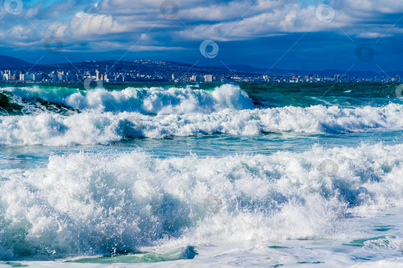Скачать Курорт Кабардинка. Черное море. Большие штормовые волны изумрудного цвета накатывают на берег. Множество брызг и пены. Порт Новороссийск и Кавказские горы на горизонте фотосток Ozero