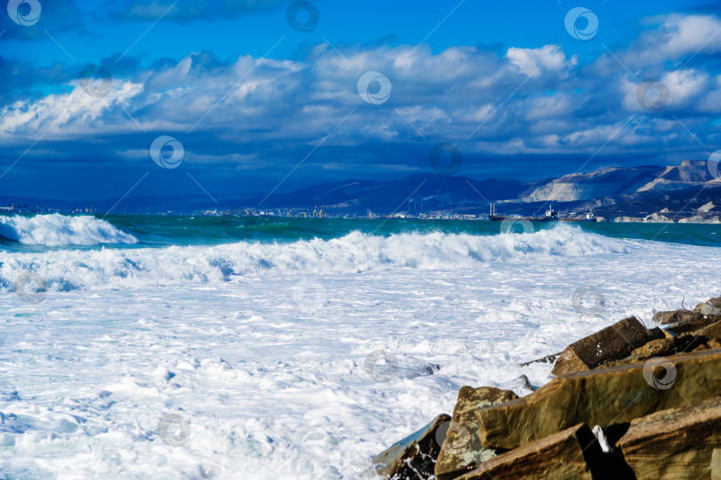 Скачать Курорт Кабардинка. Большие зеленые штормовые волны в белой пене накатываются на каменистый пляж Кабардинки. На заднем плане - порт Новороссийск и Кавказские горы. фотосток Ozero