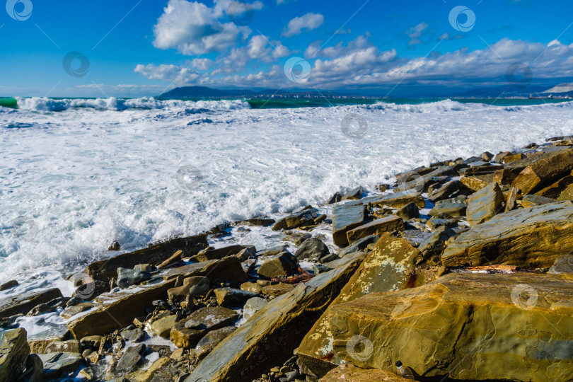 Скачать Курорт Кабардинка. Большие зеленые штормовые волны в белой пене накатываются на каменистый пляж Кабардинки. На заднем плане - порт Новороссийск и Кавказские горы. Большие камни на берегу фотосток Ozero