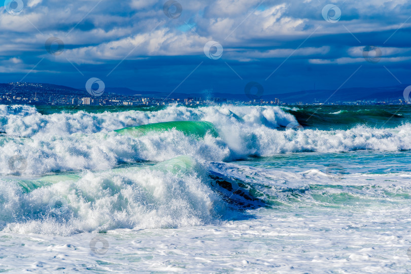 Скачать Курорт Кабардинка. Черное море. Большие штормовые волны изумрудного цвета накатывают на берег. Множество брызг и пены. Порт Новороссийск и Кавказские горы на горизонте фотосток Ozero