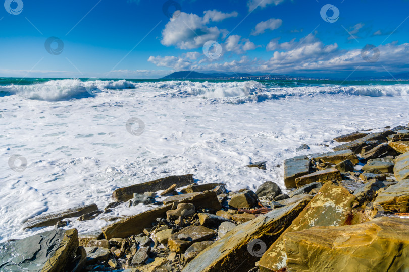 Скачать Курорт Кабардинка. Большие зеленые штормовые волны в белой пене накатываются на каменистый пляж Кабардинки. На заднем плане - порт Новороссийск и Кавказские горы. Большие камни на берегу фотосток Ozero